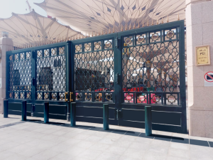 One of the gates of Madinah Al-Munawarah Mosque, featuring intricate black ironwork with gold accents and crash-rated bollards installed in front for enhanced security.