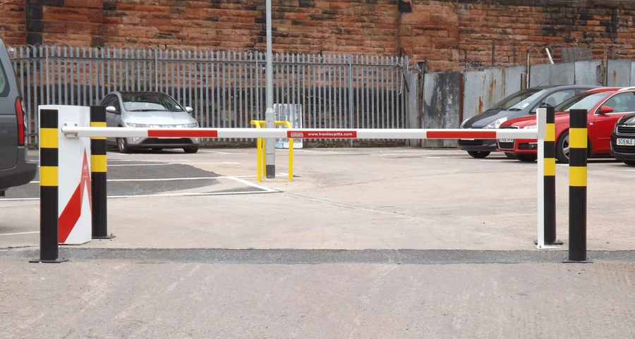 Automatic vehicle access barrier controlling entry to a secured parking area with safety bollards.
